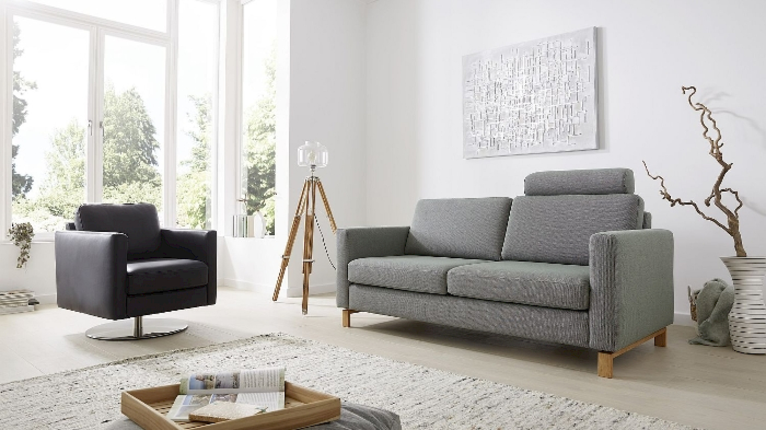 Blick in einen hellen Wohnbereich, der mit einem grauen Sofa, einem schwarzen Sessel und einem hellen Teppich eingerichtet ist